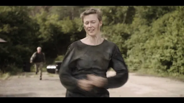 Eine Frau läuft eine Landstraße entlang, im Hintergrund folgt ein Mann