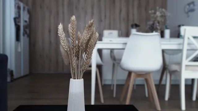 Getrocknete Weizenähren in einer weißen Vase, dahinter ein heller Essbereich mit weißen Stühlen