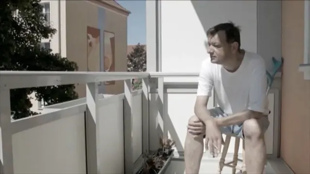 Ein Mann sitzt rauchend auf einem sonnigen Balkon