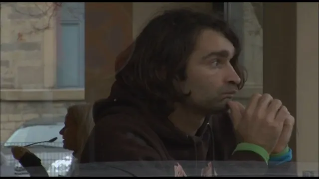 Ein Mann mit langen Haaren sitzt nachdenklich hinter einer Glasscheibe