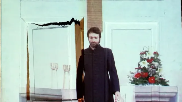 Ein Mann im dunklen Mantel vor einer gemalten Kirchenkulisse
