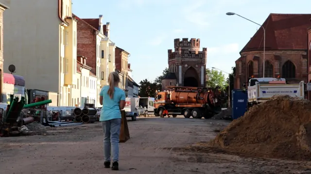Ein Mädchen geht über eine Baustelle auf ein mittelalterliches Stadttor zu