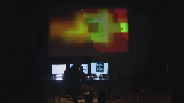 Ein Mann sitzt im Dunkeln vor Monitoren, darüber eine farbige Pixelprojektion